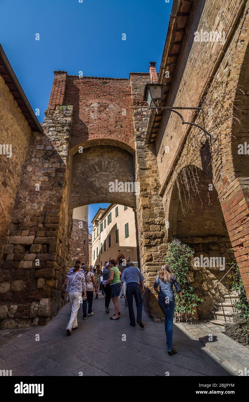 MONTEPULCIANO, ITALIEN - 15. APRIL 2013: Touristen gehen unter dem alten Backsteinbogen in Montepulciano, Toskana, Italien Stockfoto