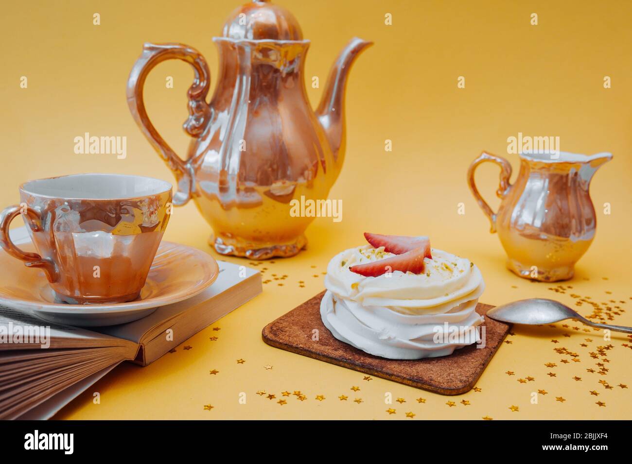 Heller und schöner Snack. Weißer Kuchen aus Baiser, Sahne und frischen Erdbeeren und Golden Tea Utensilien: Eine Tasse, eine Teekanne und ein Behälter für Kre Stockfoto