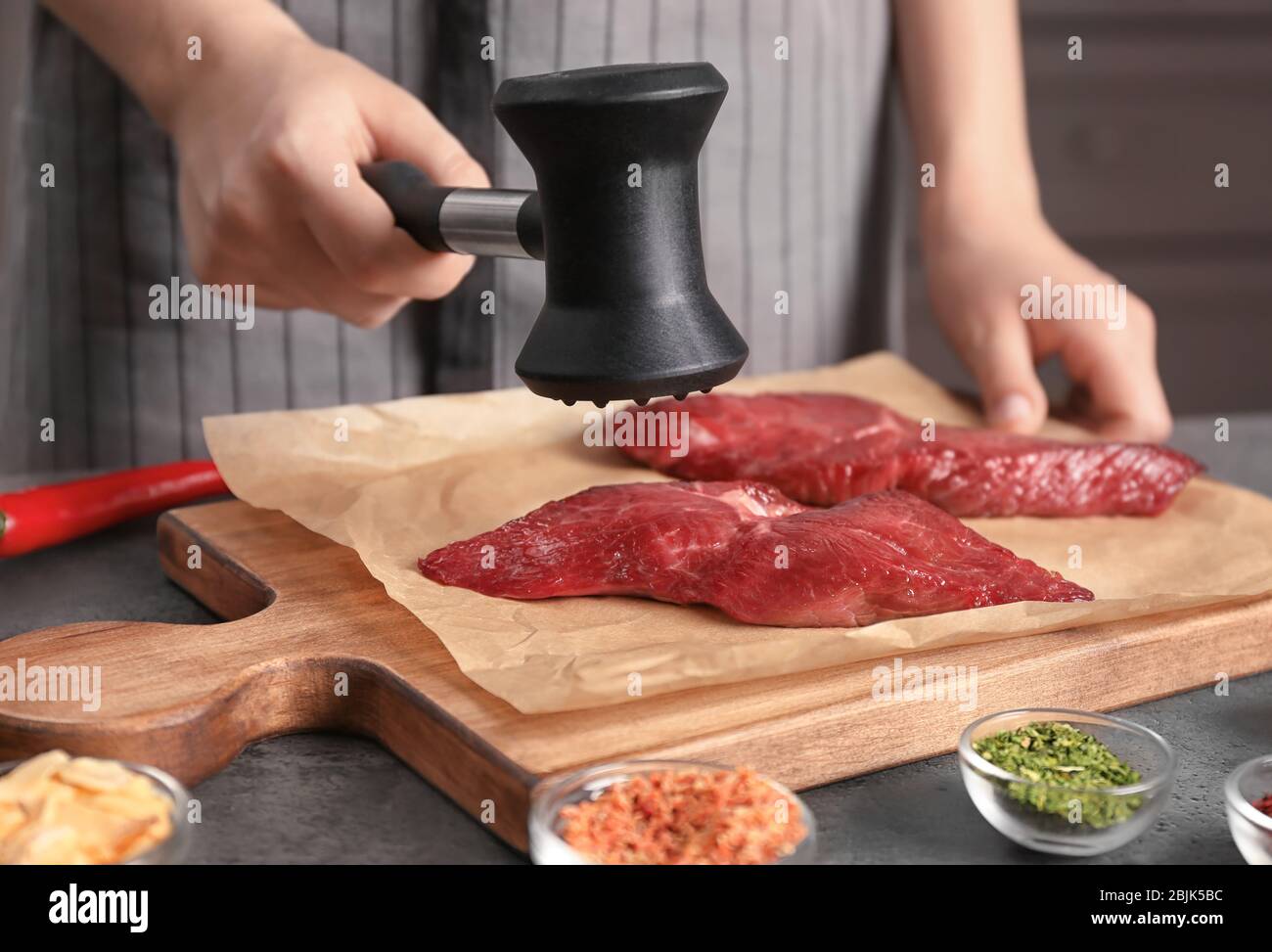 Frau schlägt rohes Steak mit Fleischhammer in der Küche Stockfoto