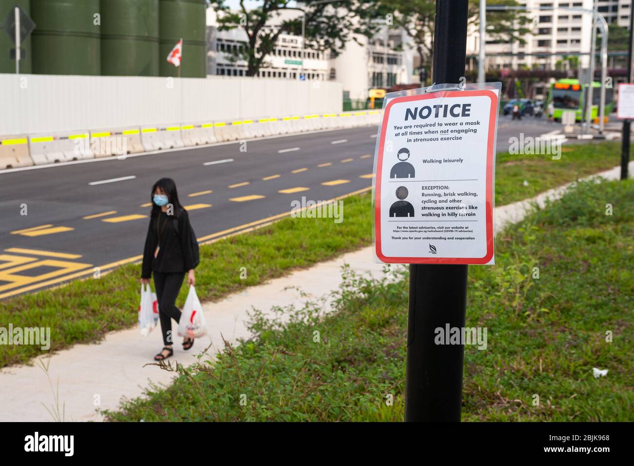 29.04.2020, Singapur, Republik Singapur, Asien - EINE Frau bedeckt ihr Gesicht mit einer schützenden Gesichtsmaske und geht an einer Notiz auf Covid-19 vorbei. Stockfoto