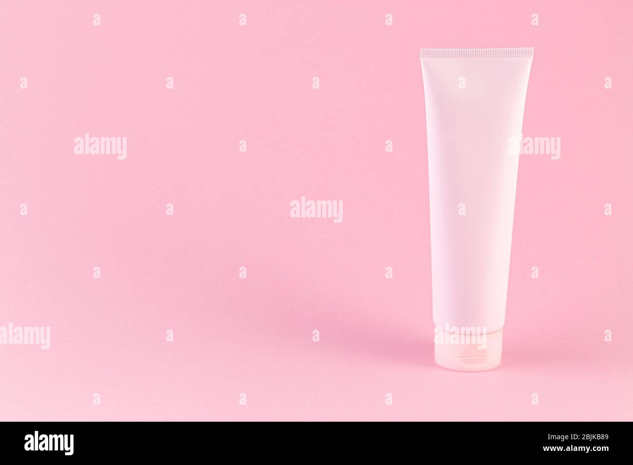 Plastikröhre mit Gesicht oder Körper Creme auf pastellrosa Hintergrund mit Kopierraum. Pastell rosa kosmetische Röhre auf dem Hintergrund des gleichen Tons. Karosserie Stockfoto