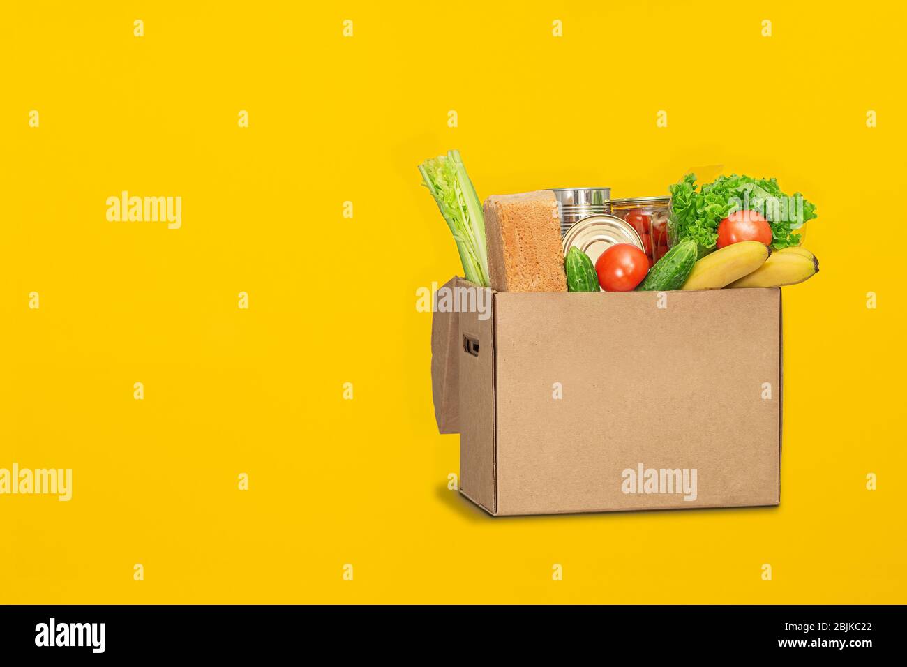 Spendenbox mit Lebensmitteln auf gelbem Hintergrund. Coronavirus Lebensmittel Lieferung. Freiwilliger bringt eine Schachtel mit Essen. Spende, Quarantäne Konzept. Freiwillige Kolle Stockfoto