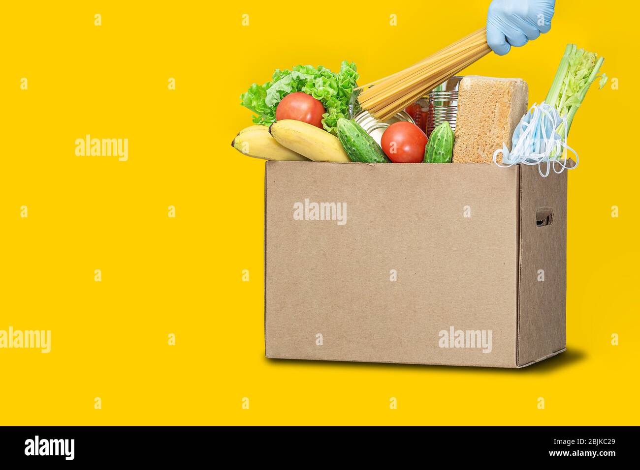 Spendenbox mit Lebensmitteln auf gelbem Hintergrund. Coronavirus Lebensmittel Lieferung. Freiwilliger bringt eine Schachtel mit Essen. Spende, Quarantäne Konzept. Freiwillige Kolle Stockfoto