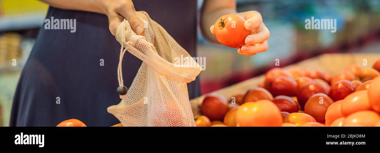 Eine Frau wählt Tomaten in einem Supermarkt ohne Plastikbeutel. Wiederverwendbare Tasche für den Kauf von Gemüse. Banner für Zero Waste Concept, LANGES FORMAT Stockfoto