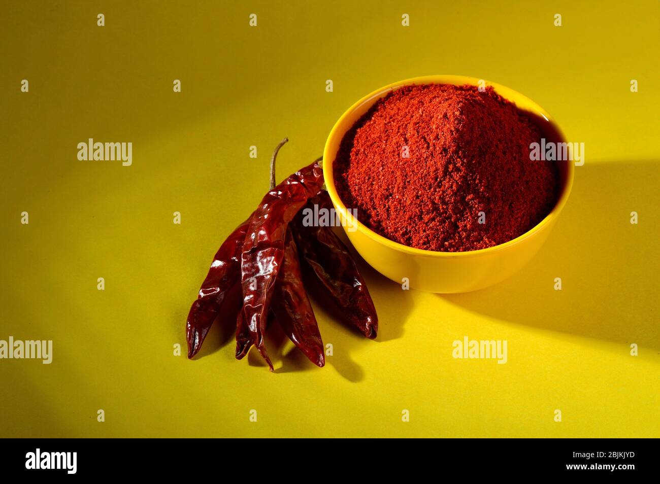 Chilipulver in gelber Schüssel auf gelbem Hintergrund. Rote, kalte Paprika. Stockfoto