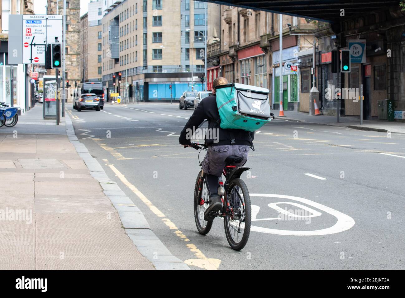 Deliveroo Rider, der während der Sperrung des Coronavirus durch die fast menschenleeren Straßen von Glasgow, Schottland, Großbritannien, radelt Stockfoto