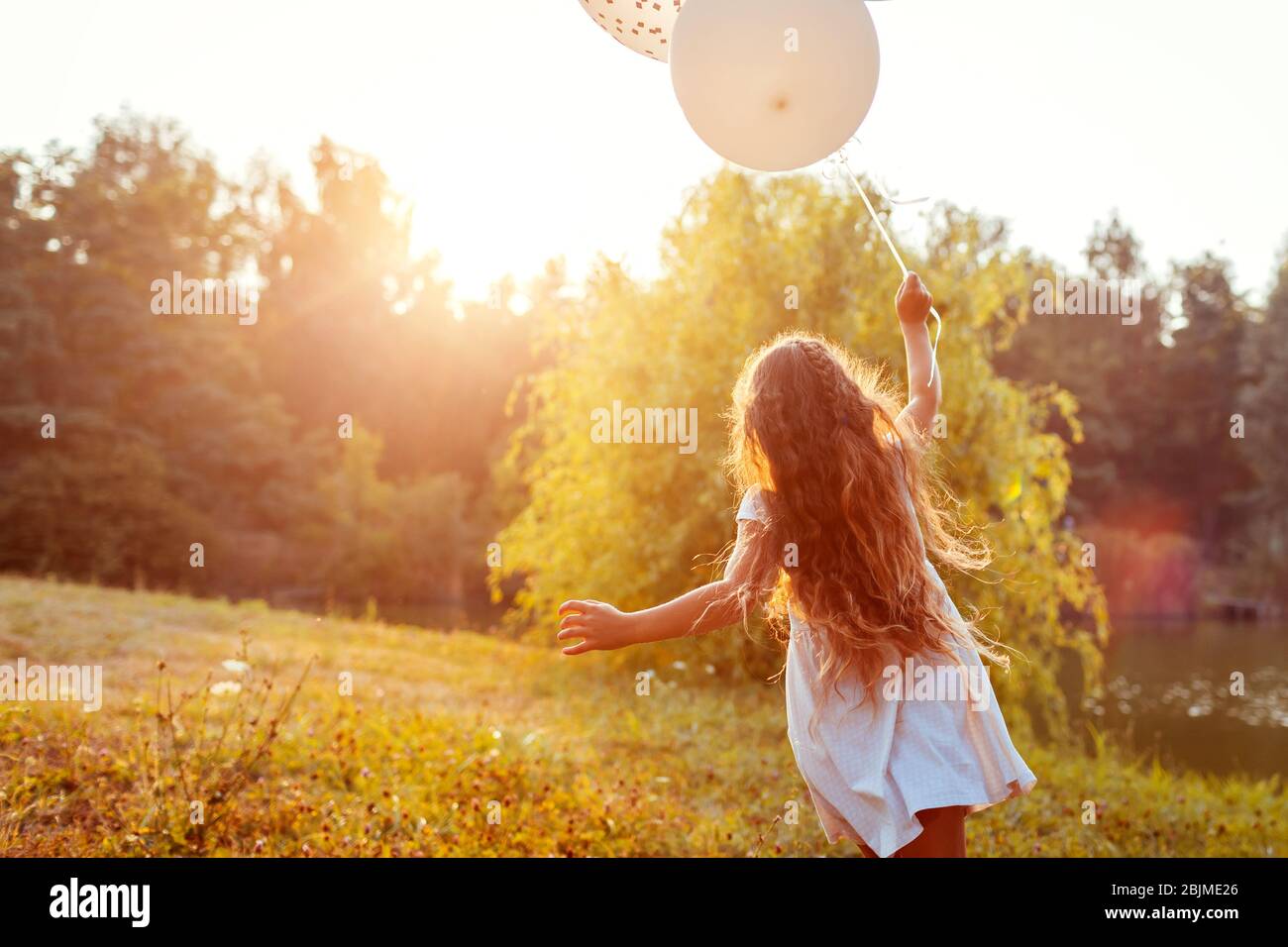 Hübsches kleines Mädchen, das mit Ballonen in der Hand läuft. Kind mit Spaß im Sommerpark. Aktivitäten im Freien Stockfoto