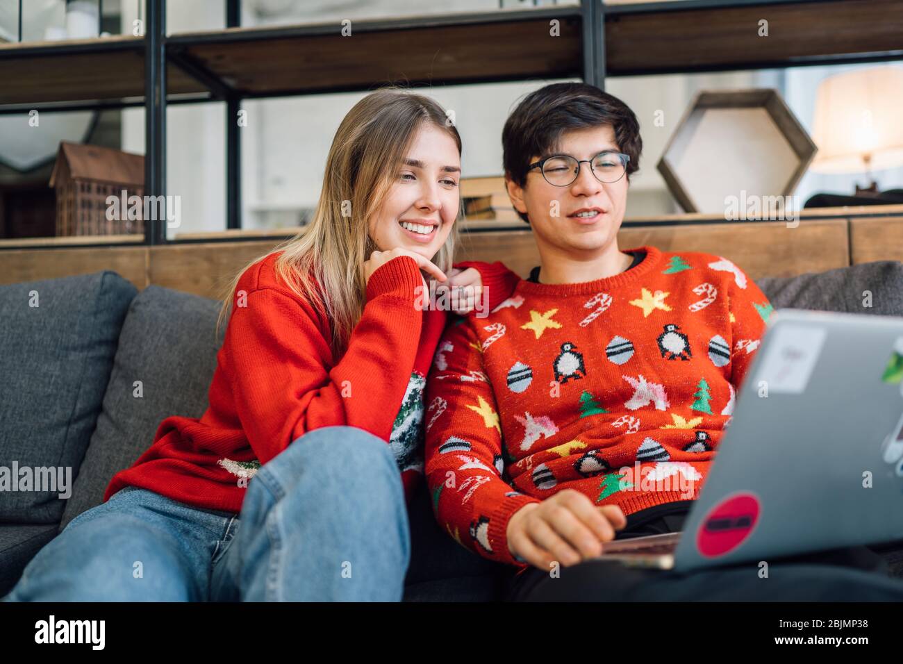 Glückliches Paar mit Laptop zusammen auf dem Sofa, lächelndes junges Mädchen und Kerl, die Spaß haben, zu Hause zu sprechen Stockfoto