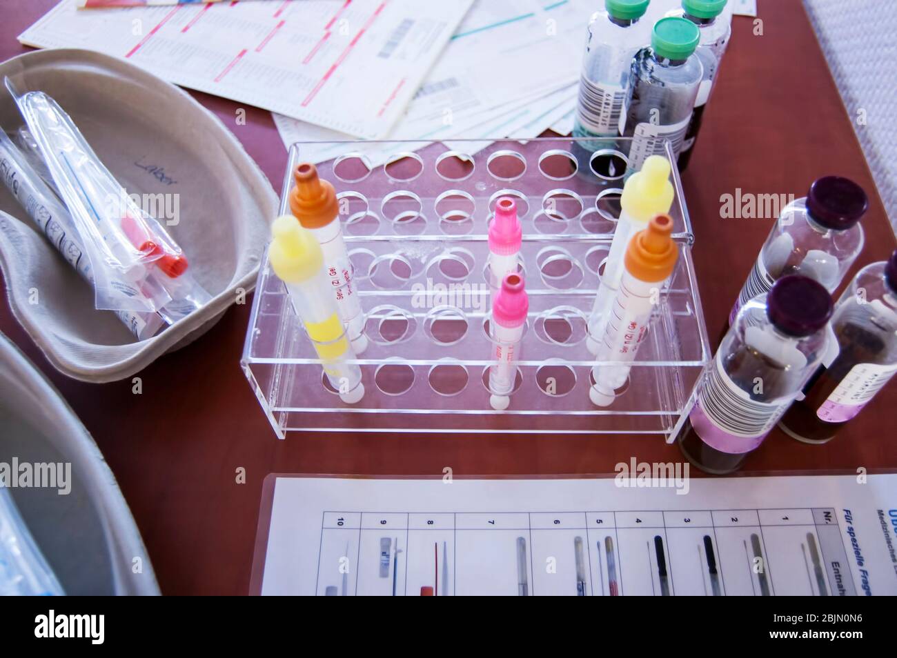 Rack mit Blutgefäßen mit Barcode-Etiketten zur korrekten Identifizierung von verschiedenen Patienten. Tablett mit Röhrchen mit Blutproben, Spritze und Labor Stockfoto