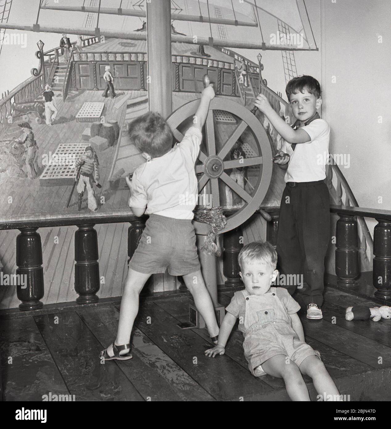 1950er Jahre, historisch, auf einem Dampfschiff der Union-Burg spielen zwei kleine Kinder in der Kinderstube des Schiffes auf dem Deck eines Holzbootes, spielen das hölzerne Spielzeugruder. Stockfoto