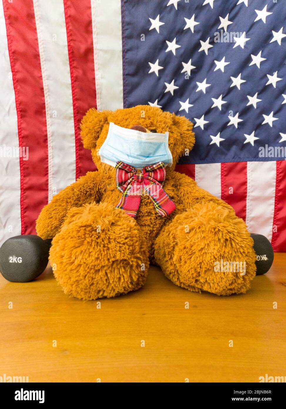 Teddybär mit Gesichtsmaske und Kurzhanteln. Flagge der USA Stockfoto