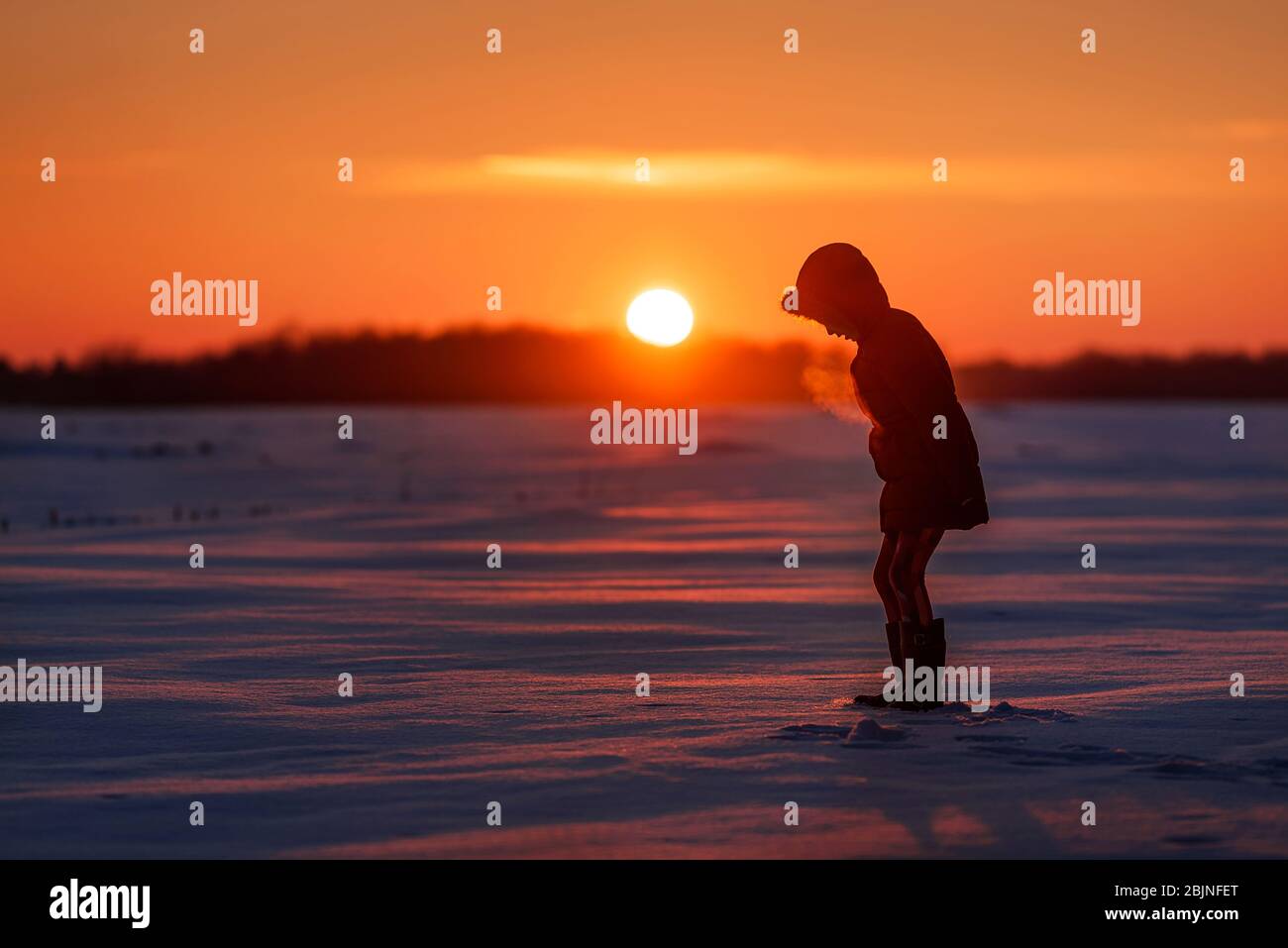 Silhouette eines Mädchens, das bei Sonnenuntergang in einem verschneiten Feld in den USA steht Stockfoto