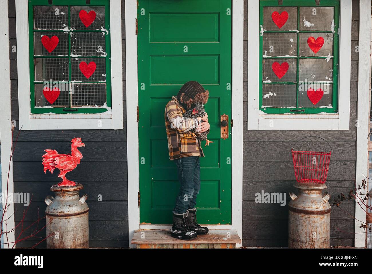 Junge, der vor einem Hühnerstall steht, umarmt ein Huhn, USA Stockfoto