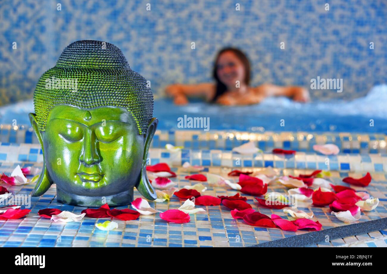 Buddha Kopf und Rosenblätter in einem Spa, junge Frau in einem Whirl-Pool im Hintergrund, Frankreich, Savoie, Sainte-Foy-Tarentaise Stockfoto