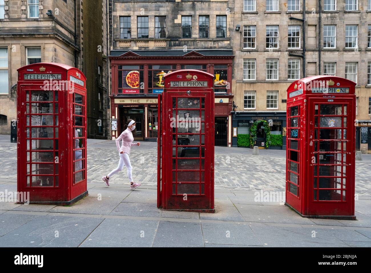 Joggingin mit Gesichtsmaske, die während der Sperrung des Coronavirus in der Edinburgh Old Town, Schottland, Großbritannien, entlang der leeren Royal Mile läuft Stockfoto