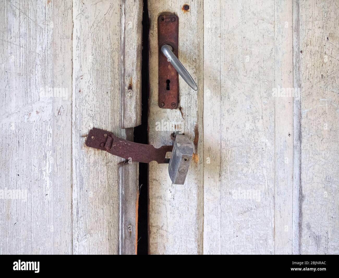 Teil einer alten verwitterten Außendoppeltüren mit einer Lücke. Beschädigte weiß lackierte Holzoberfläche, alter Eisengriff, leeres Schlüsselloch, Scharnier Stockfoto