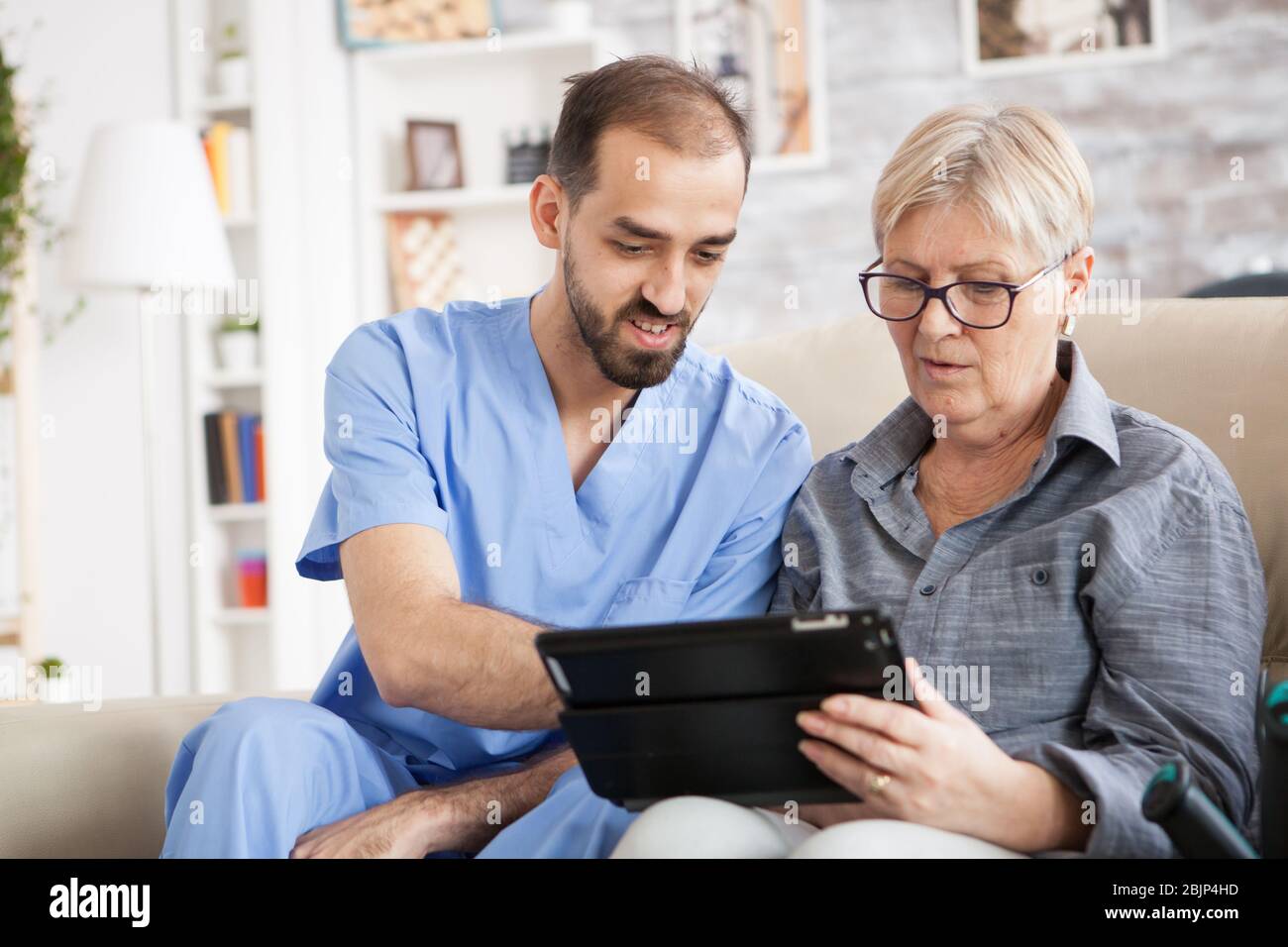 Gesundheitsbesucher, die älteren Frauen helfen, Tablet im Pflegeheim zu verwenden. Stockfoto