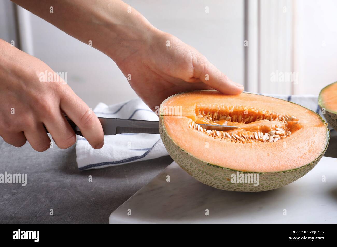 Frau schneidet Melone auf Küchentisch Stockfoto