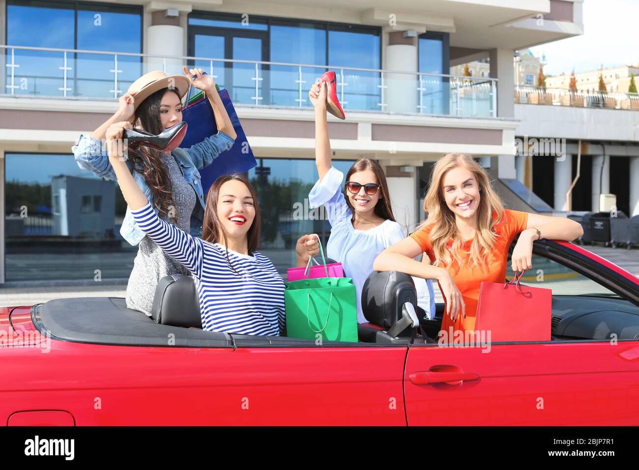 Schöne junge Frauen mit Einkaufstaschen im Cabrio im Freien Stockfoto