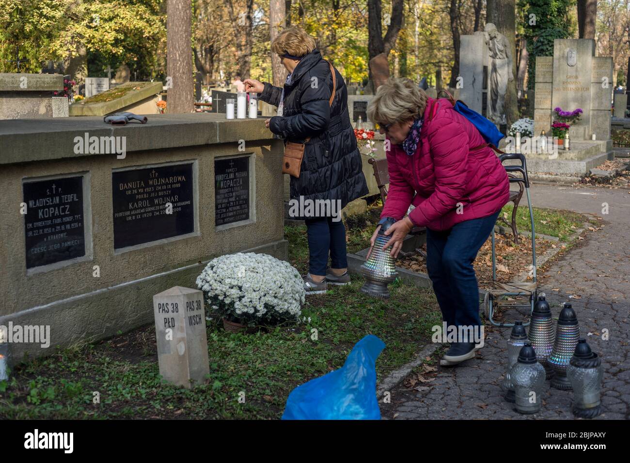 Zwei Frauen pflegen 2019 auf dem Rakowicki-Friedhof in Krakau, Polen, ein Grab mit Blumen und Kerzen. Stockfoto