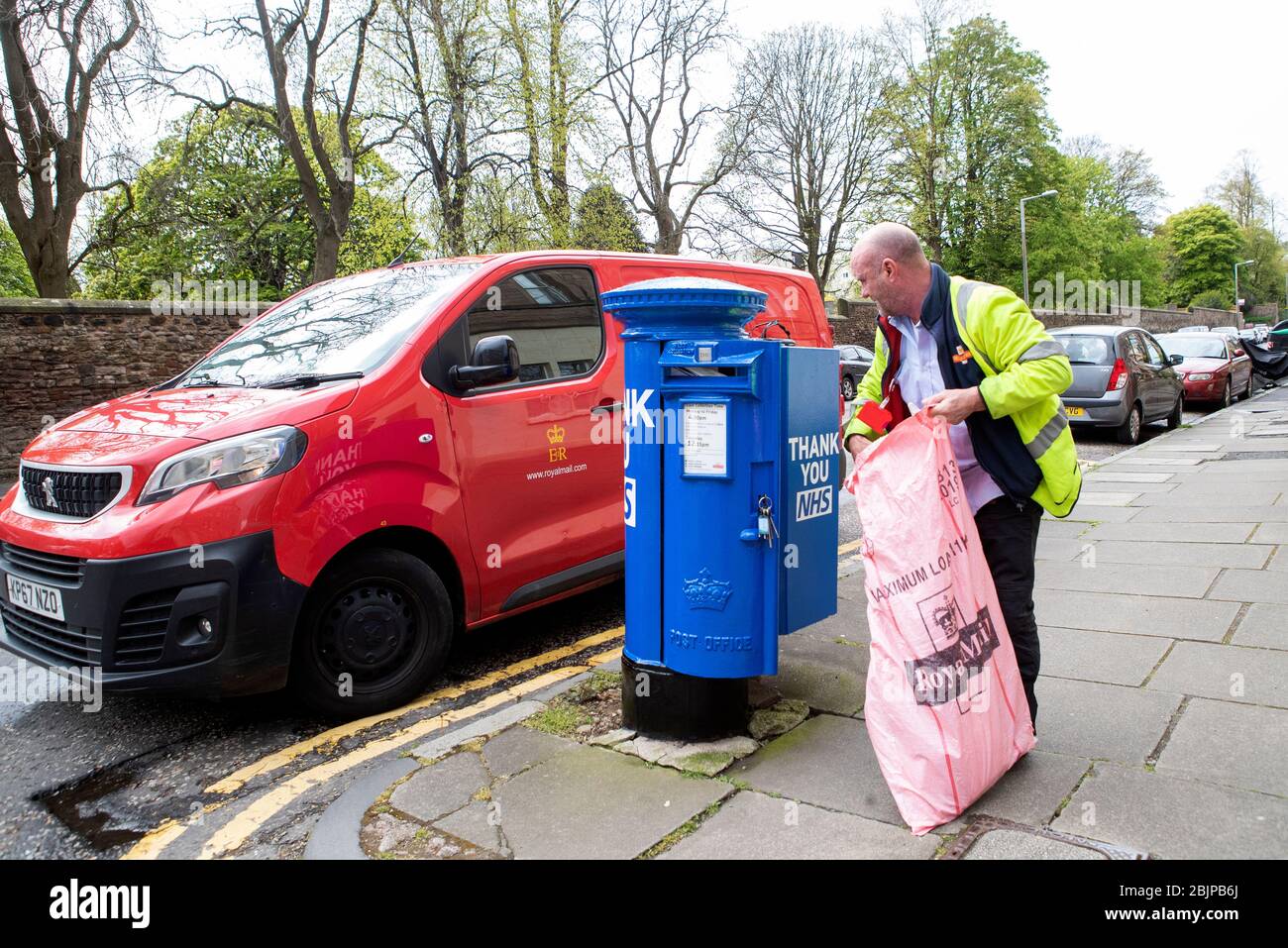 Ein Postbote leert einen der speziell dekorierten Briefkästen in Edinburgh, die blau gestrichen wurden, um die NHS-Arbeiter und Betreuer zu unterstützen, die gegen die Coronavirus-Pandemie kämpfen. Stockfoto
