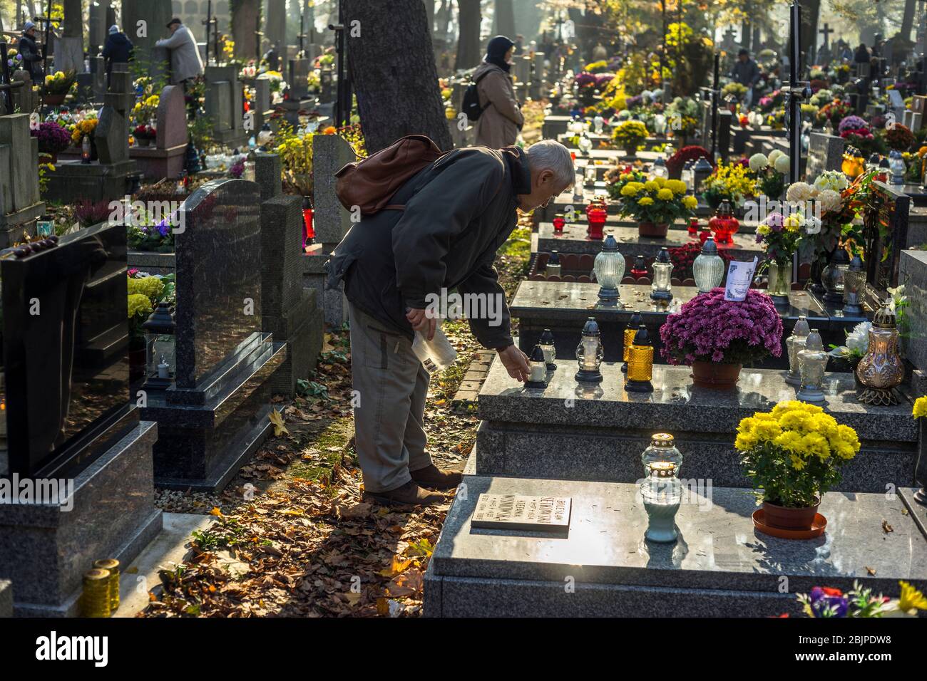 Ein Mann stellt eine Kerze auf ein Grab eines verstorbenen geliebten Menschen auf dem Rakowicki Friedhof in Krakau, Polen 2019. Stockfoto