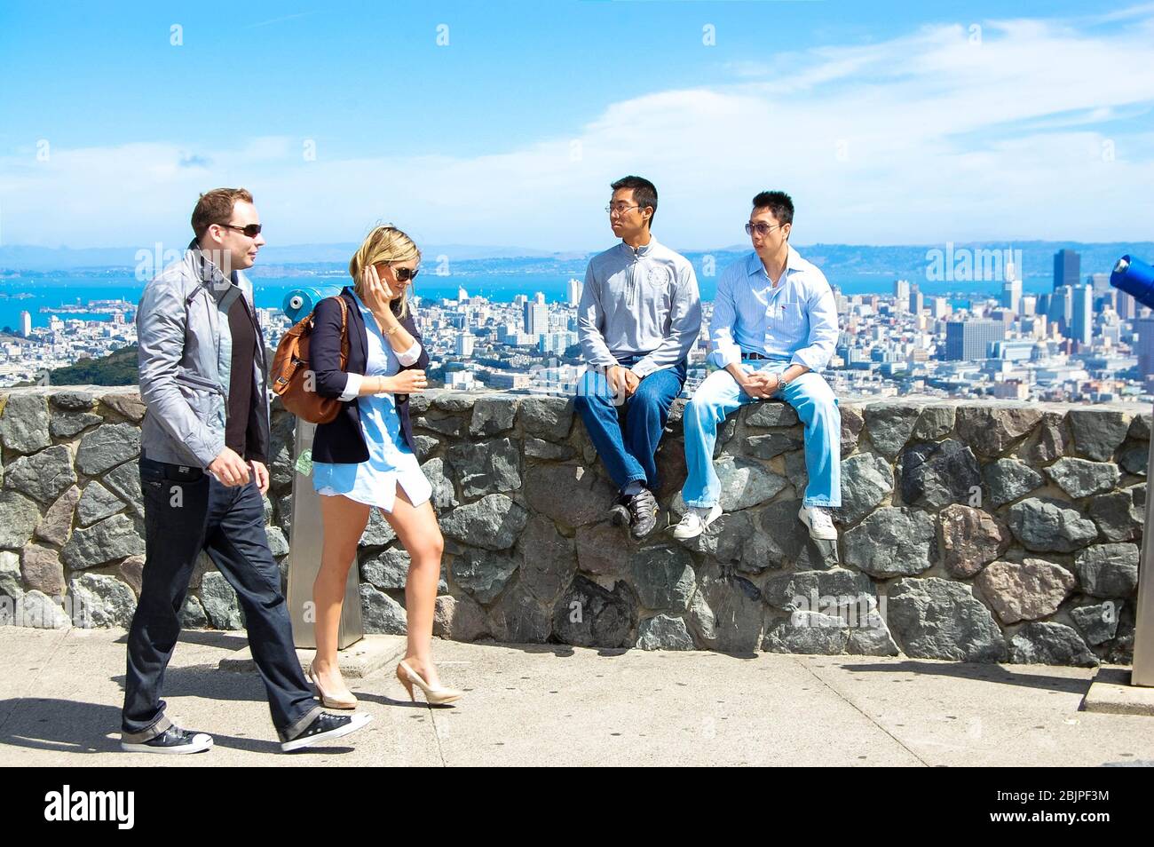 San Francisco Beine hübsches blondes Mädchen mit Blick auf die Bucht von San Francisco Wasser zwei Männer sitzen auf einer Mauer Wolkenkratzer Stockfoto