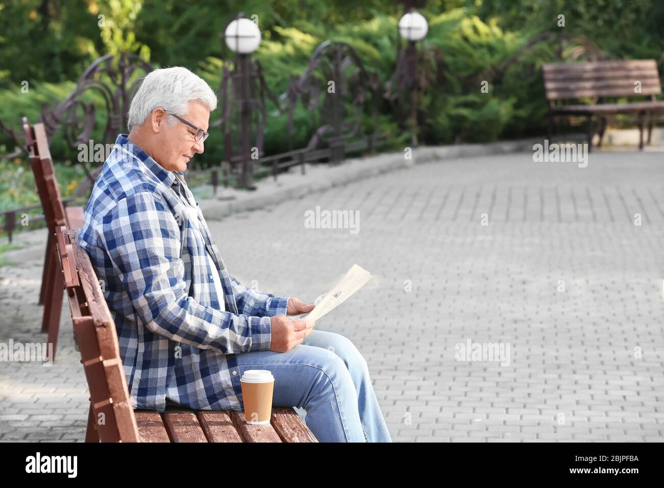 Schöner reifer Mann liest Zeitung auf Bank im Park Stockfoto