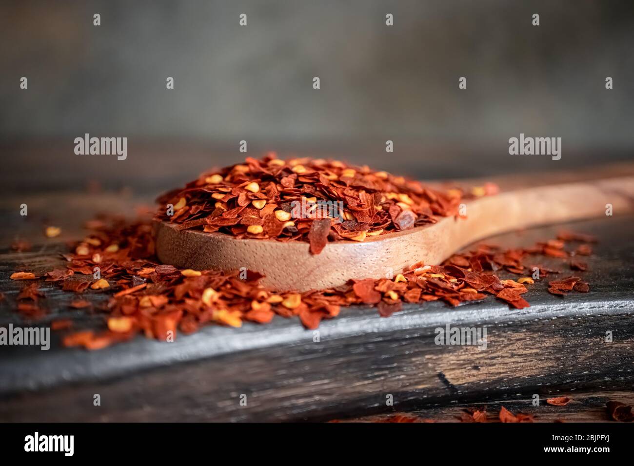 Flocken von roten Chili Chili in Holzlöffel Nahaufnahme auf einem Küchentisch. Stockfoto