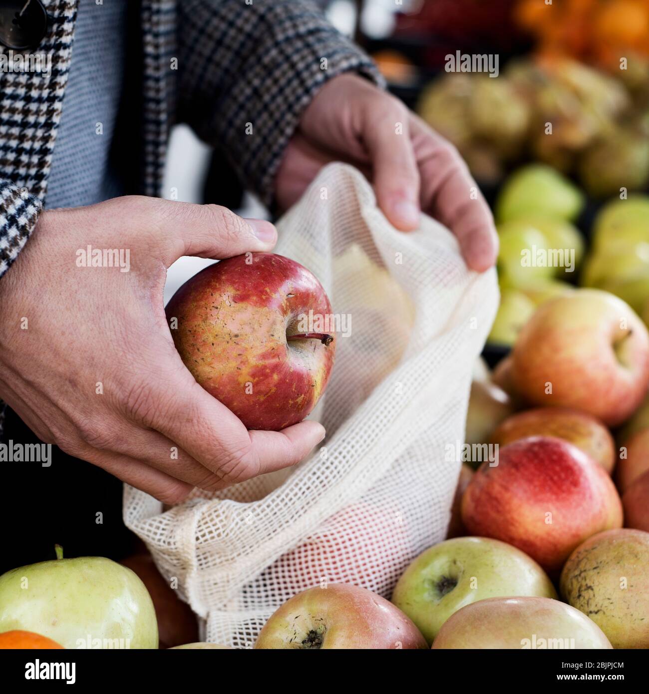 Nahaufnahme eines Mannes, der in einem Gemüsehändler einkaufen geht, indem er einige Äpfel in einen wiederverwendbaren Stoffbeutel legt, um die Plastikverschmutzung zu verringern Stockfoto