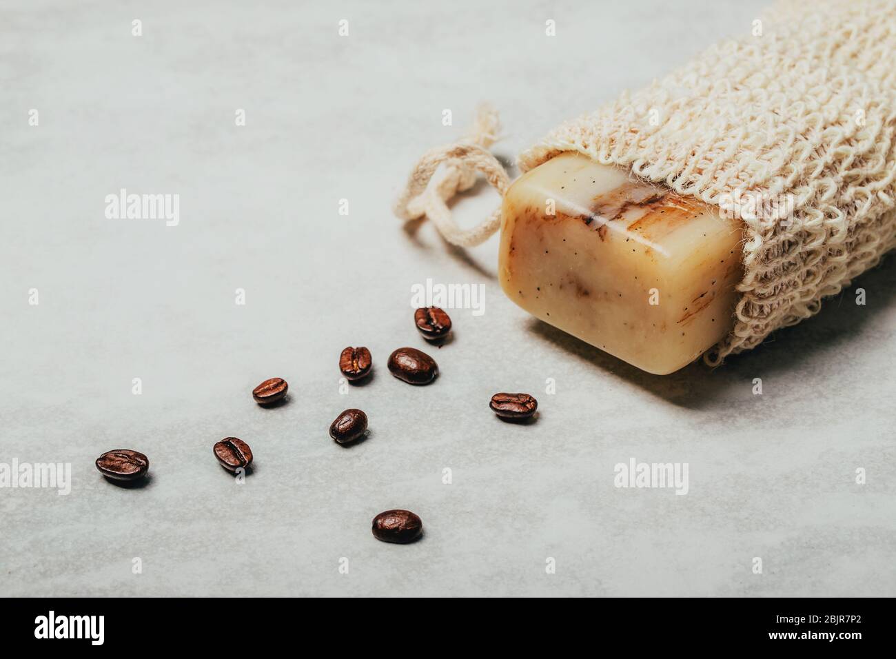 Stück Seife in Naturbeutel mit Kaffeebohnen auf rustikalem grauen Hintergrund. Gesundheits- und Schönheitskonzept. Stockfoto
