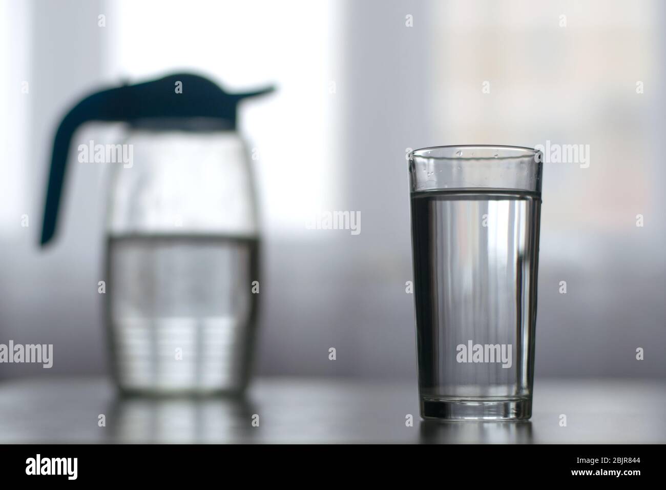 Ein Glas mit Wasser und eine Karaffe im grauen Hintergrund Stockfoto