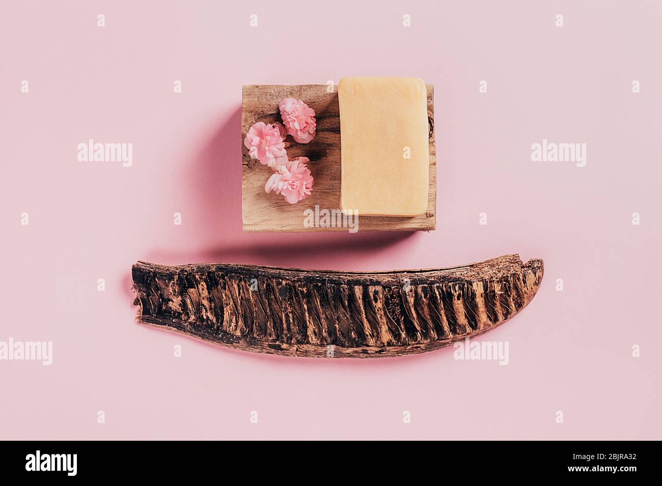 Stück Seife auf Holzbalken mit Begonia Blumen auf rosa Papier Hintergrund. Gesundheits- und Schönheitskonzept. Stockfoto
