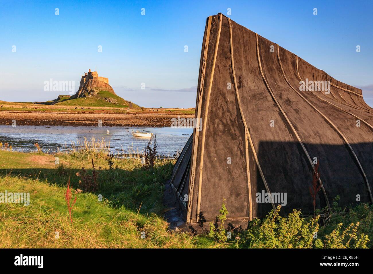 Ein umgedrehter Bootsrumpf am Ufer der Holy Island mit Lindisfarne Castle im Hintergrund, England Stockfoto