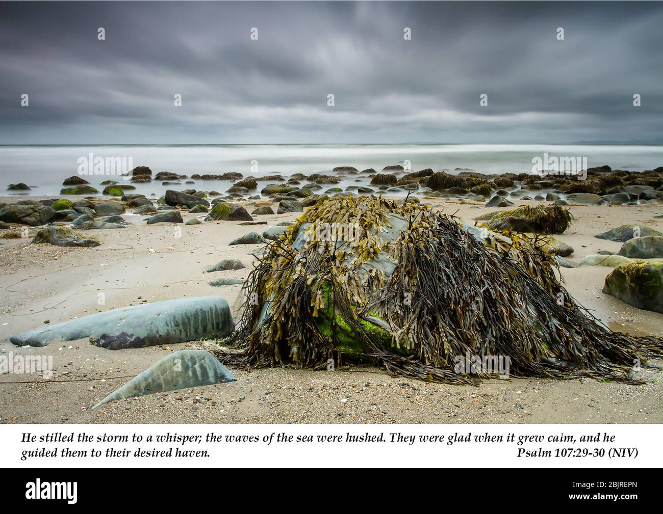 Sturmwolken über dem Shell Beach mit Algen bedeckten Felsen im Vordergrund mit christlicher Schrift aus Psalm 107:29-30 aus dem Alten Testament. Stockfoto