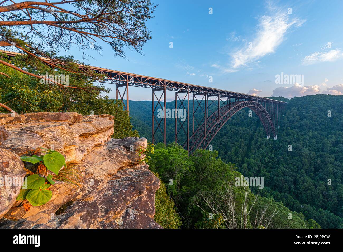 Die große Stahlbogenbrücke der New River Gorge überspannt den Canyon unter einem blauen Himmel, der von der Felswand eines Klettergebiets aus gesehen wird. Stockfoto