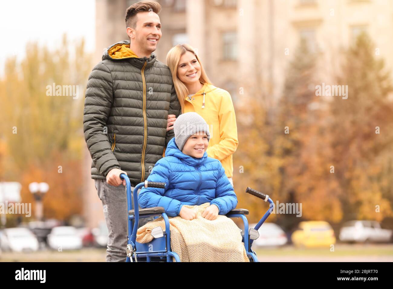 Pärchen mit ihrem kleinen Sohn im Rollstuhl draußen am Herbsttag Stockfoto