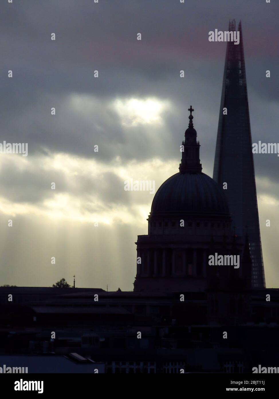 Lichtstrahlen, die Gedankenlücken in der Wolkendecke mit den Silhouetten der St. Paul-Kuppel und der Shard im Vordergrund, London, Großbritannien, leuchten Stockfoto