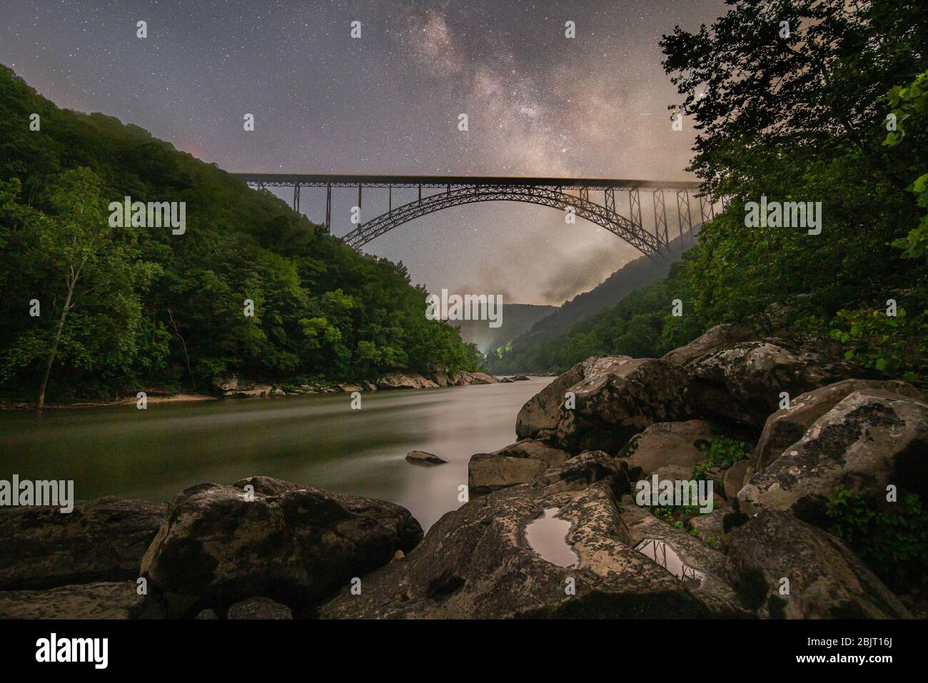 Die Nacht wird in der New River Gorge lebendig, während die Milchstraße über der legendären Bogenbrücke aufsteigt, die Berghänge Nebelschwaden und Glühwürmchen ausatmen Stockfoto