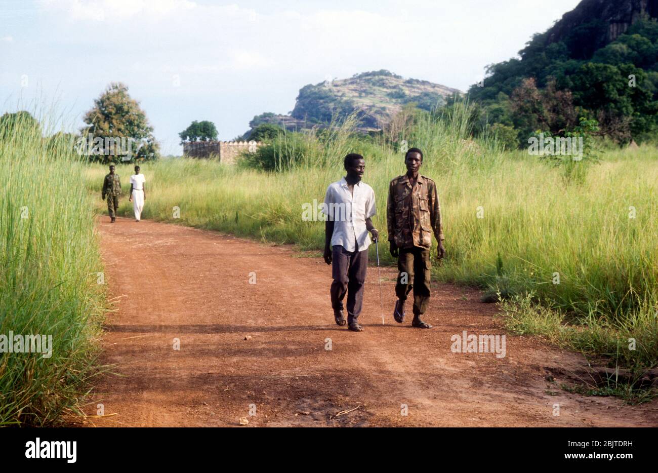 Sudanesische Zivilisten und SPLA-Armeeangehörige gehen in einem Dorf in der Nähe von Yei, Republik Südsudan, auf einer unbefestigten Straße Stockfoto