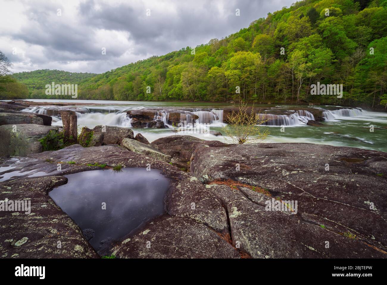 Die bewölkten Regenwolken können in einem Pool von Wasser aus einem Felsvorsprung mit Blick auf die Fälle von Valley Falls State Park auf dem Tygart reflektiert werden Stockfoto