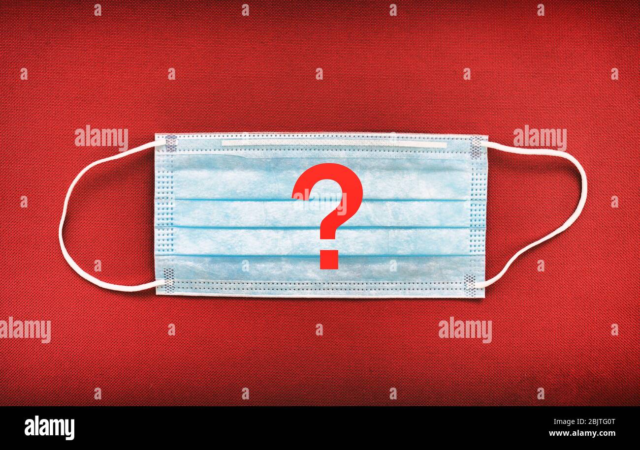COVID-19 - ist es notwendig, eine Maske zu tragen. Sollte das Tragen einer Gesichtsmaske in Städten, in denen soziale Distanzierung nicht möglich ist, obligatorisch sein. Fragezeichen auf rotem Hintergrund der Maske. Stockfoto