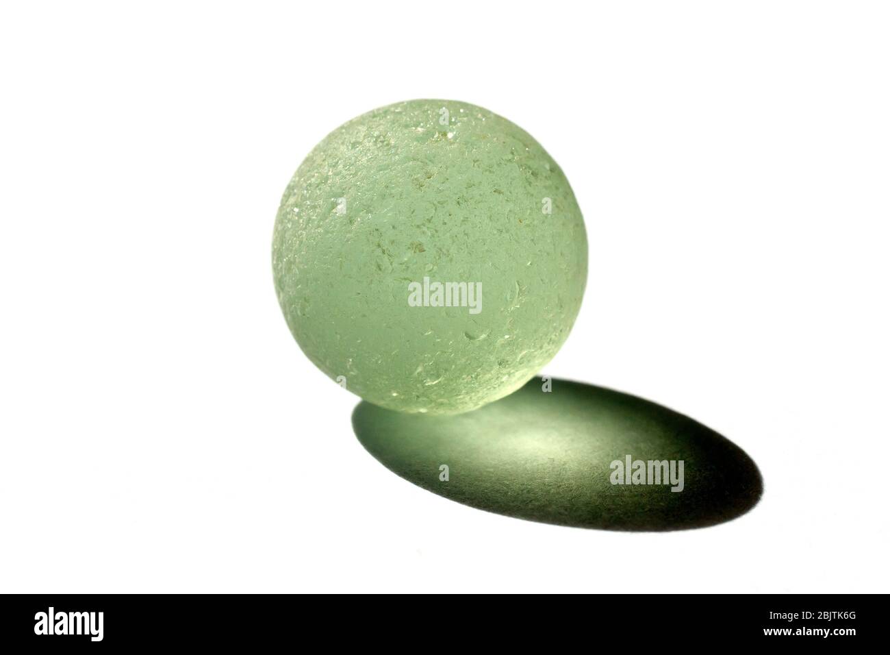 Nahaufnahme Stillleben eines gebrochenem blassgrünen Glasmarmors und der Schatten, den er in gerichtete Sonnenlicht wirft, isoliert vor weißem Hintergrund. Stockfoto