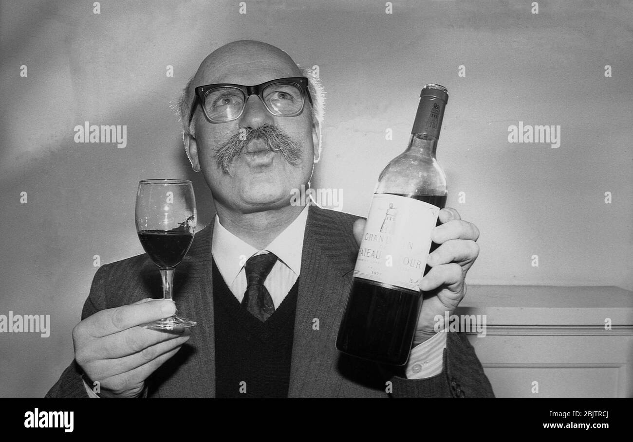 1980s, historisch, ein reifer Herr, der eine Jacke und Krawatte mit einem  buschigen Schnurrbart trägt, einen Schluck Rotwein wirbelt, eine Chateaux  La Tour von 1977, um den Geschmack oder das Bouquet zu