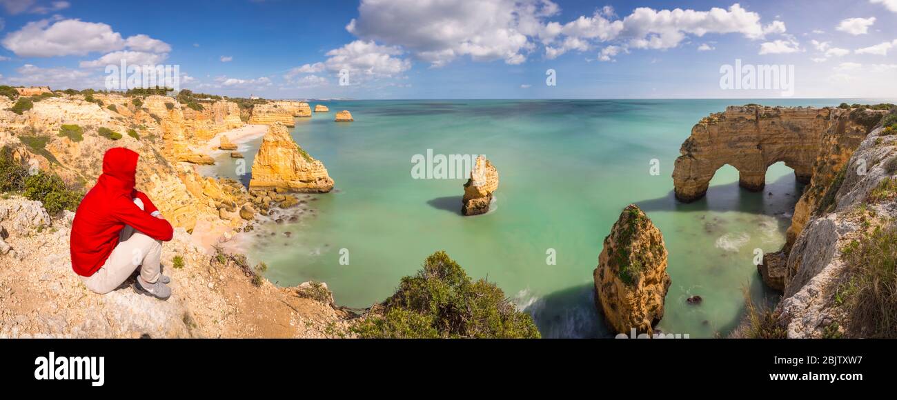 Panoramablick auf einen Mann mit Blick auf einen natürlichen Felsbogen in der Nähe von Praia da Mesquita, Lagoa, Portugal Stockfoto