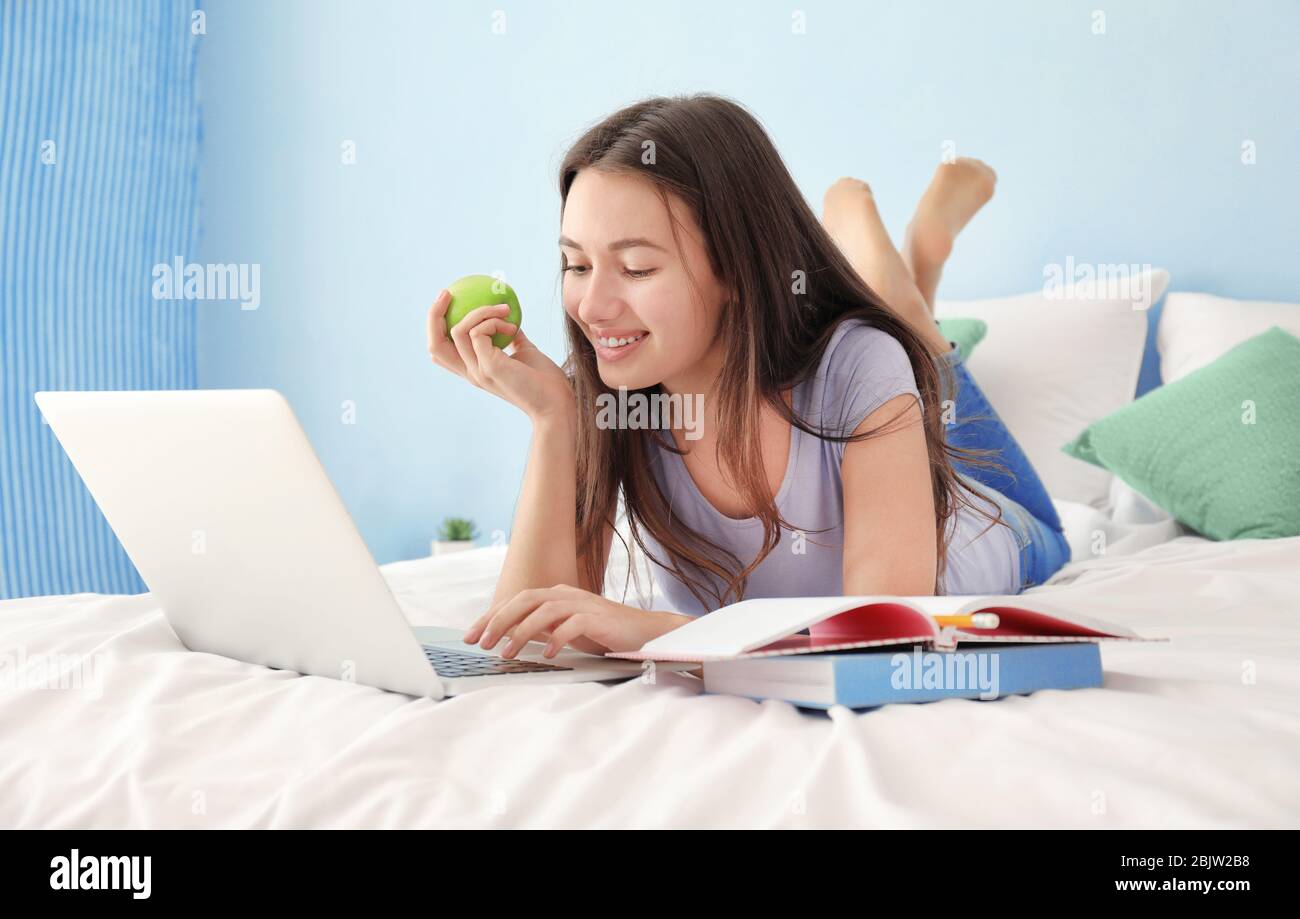 Nettes Teenager-Mädchen mit Laptop während Hausaufgaben im Schlafzimmer Stockfoto