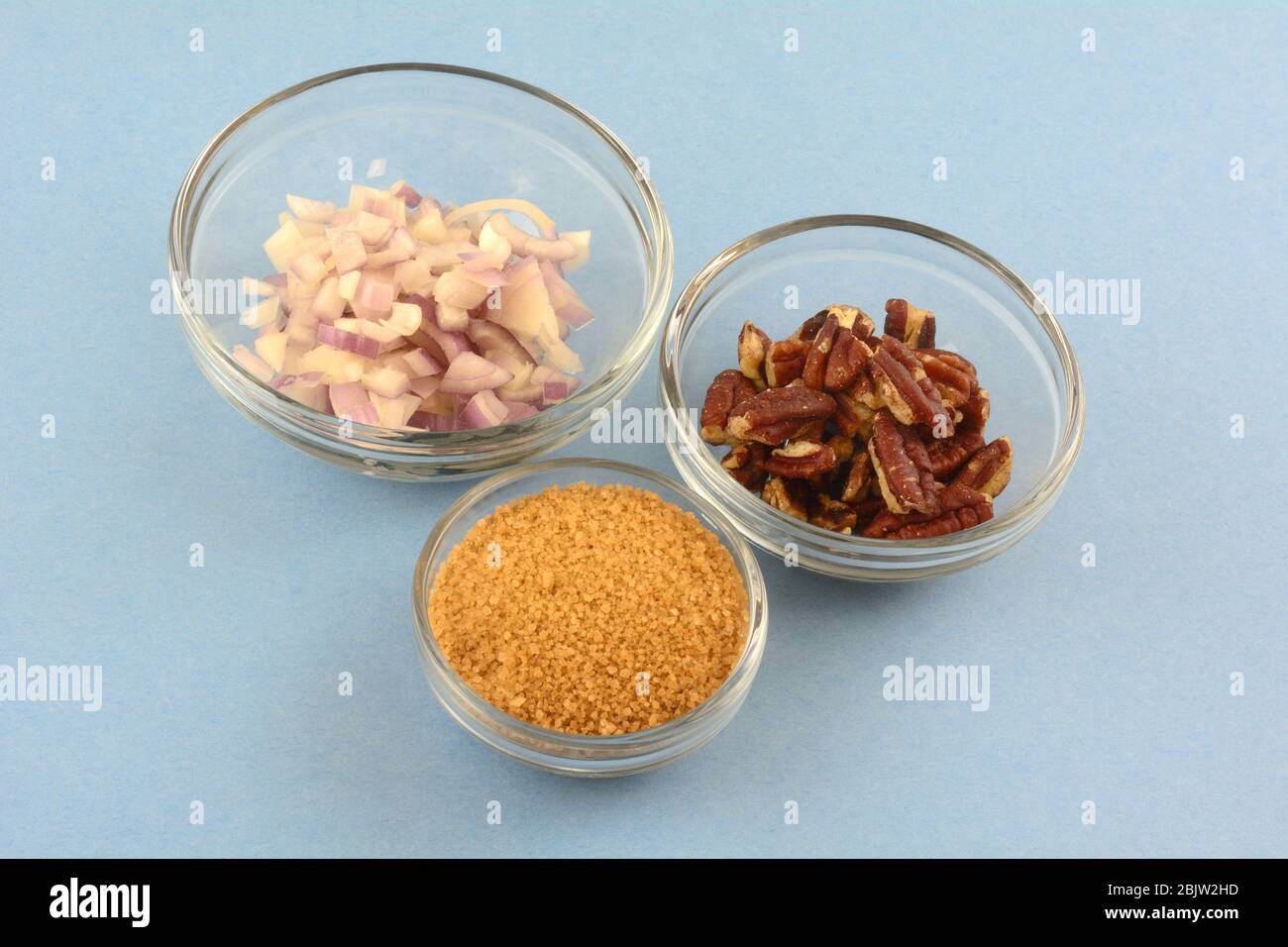 Zutaten aus gehackten Schalotte Zwiebel, brauner Zucker und Pekannüsse in Glasschüsseln zum Kochen auf blauem Hintergrund Stockfoto