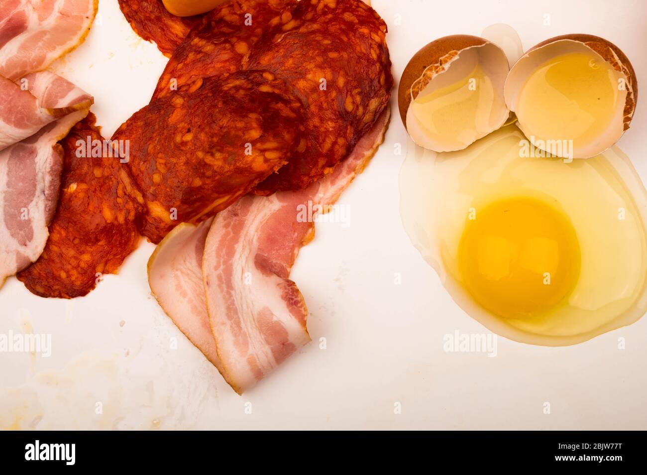 Zerbrochenes Hühnereier, Scheiben Wurst und Speck und Tomaten auf weißem Hintergrund. Nahaufnahme Stockfoto