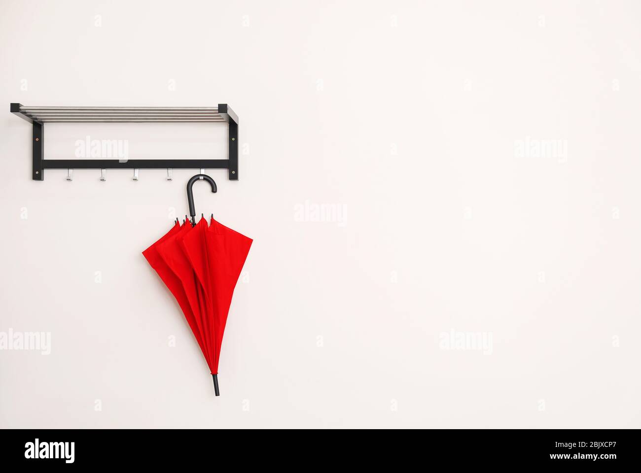 An der Wand hängt ein eleganter roter Regenschirm Stockfoto