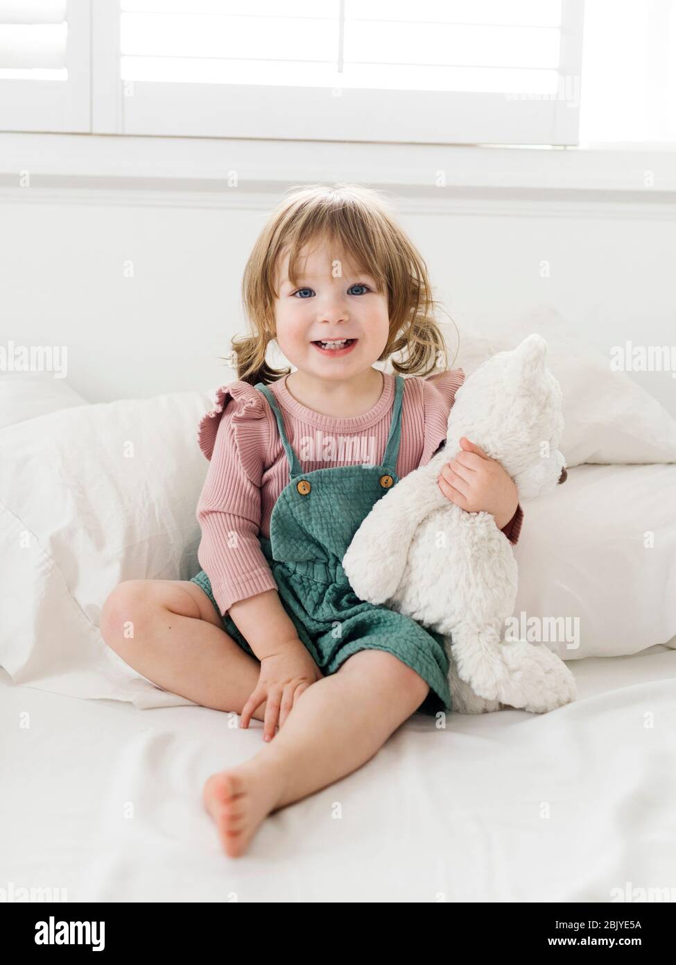 Mädchen (2-3) sitzt auf dem Bett mit Teddybär Stockfoto